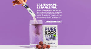 Taste Grape Less Filling, Advertisement featuring Pure Kick's new Concord Grape flavor drink mix. A hand pours the powder into a glass of water, with the mix dissolving to create a purple drink. Bunches of fresh Concord grapes and a box of the product are displayed in the foreground. The purple background carries the tagline 'TASTE GRAPE. LESS FILLING.' highlighting no extra sugar or calories. A call-to-action button says 'FIND YOUR GRAPENESS'.